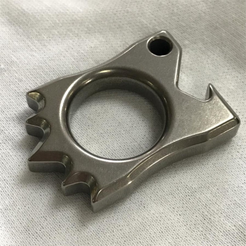Top-down view of titanium hedgehog multi-tool on white fabric, showing central ring and spike texture
