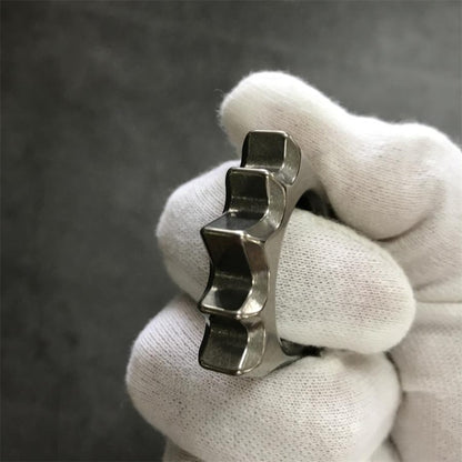 Titanium hedgehog multi-tool on grey surface showing glass breaker tip and bottle opener slot
