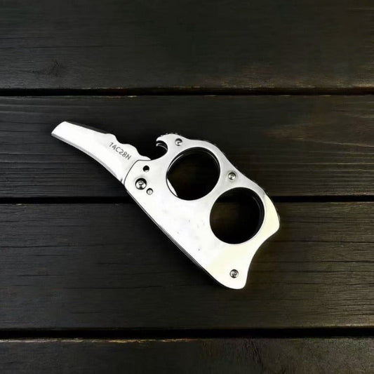 Stainless steel mini knuckle knife with hawkbill blade resting on dark wood surface