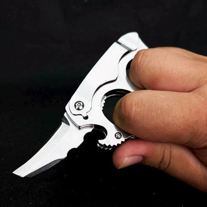 Hand holding deployed mini knuckle knife showing hawkbill blade and finger holes