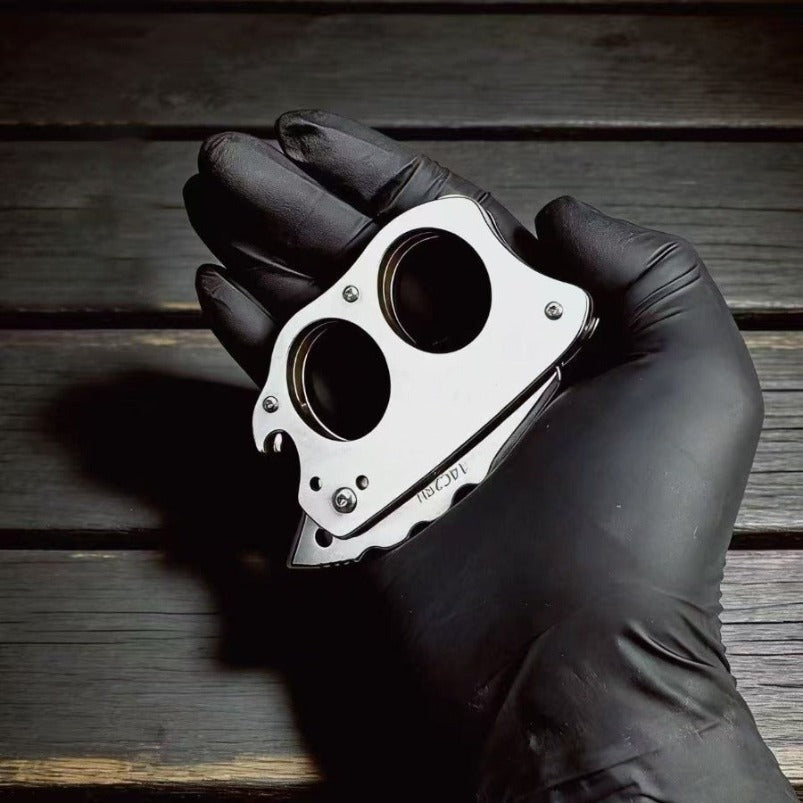 Hand in black glove holding closed mini knuckle knife showing two-finger grip