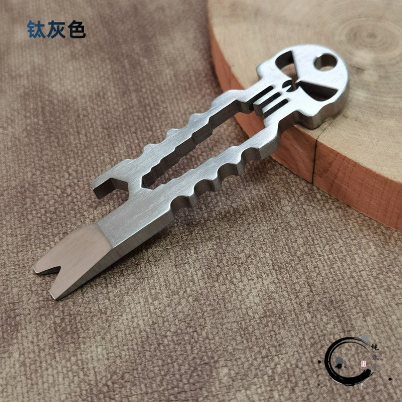 Gray titanium skull multi-tool with size measurement markings on fabric background